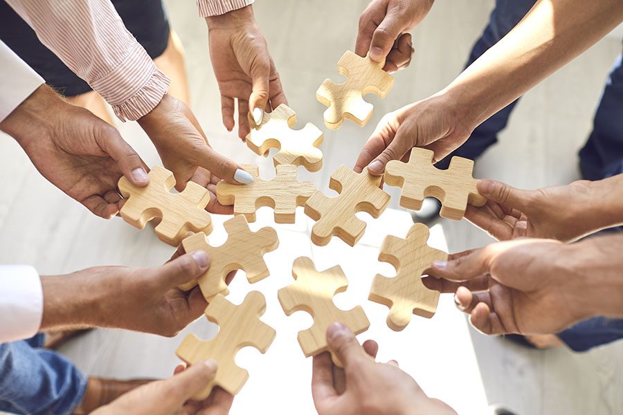 Partners - Closeup View of a Group of Business Professionals Holding Out Wooden Puzzle Pieces in Their Hands in a Huddle