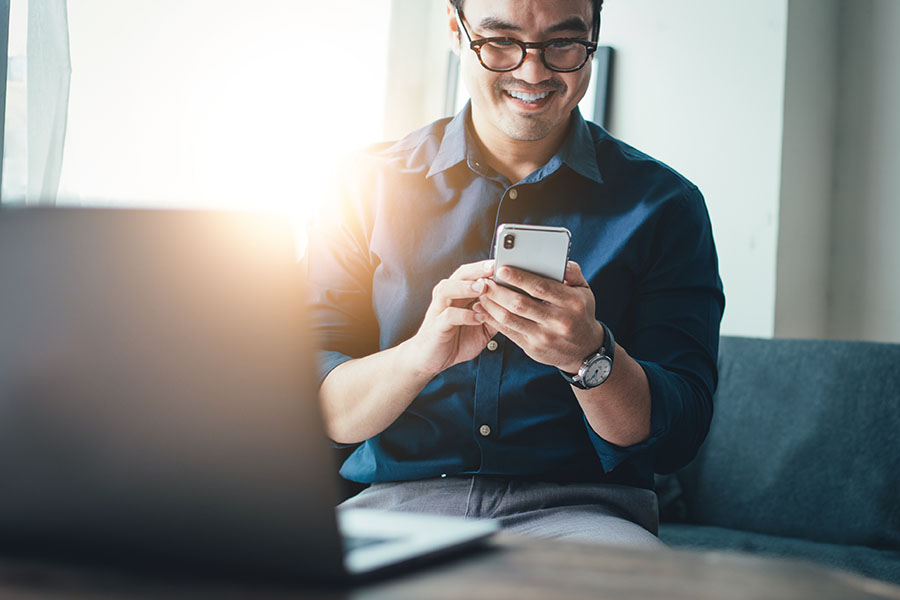 Text Message Templates - Portrait of a Cheerful Man Wearing Glasses Sitting on the Sofa While Using a Phone with a Laptop on the Coffee Table Next to Him