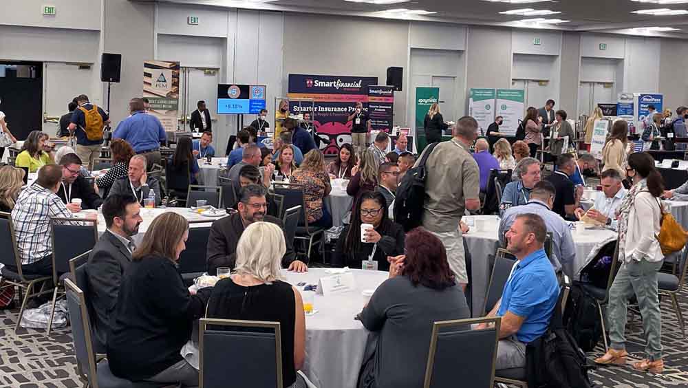 Blog - Professionals Sitting at Round Tables and Discussing While There are Open Displays for Organizations Around Them at the 2021 HUG National Conference